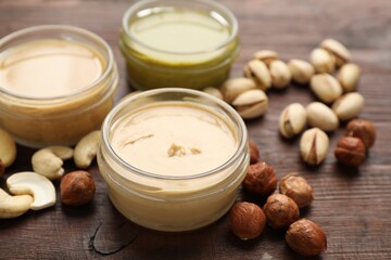 Different types of delicious nut butters and ingredients on wooden table, closeup
