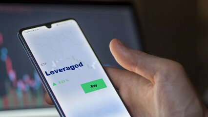 An investor's analyzing the leveraged etf fund on a screen. A phone shows the prices of Leveraged