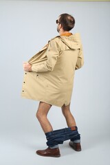 Exhibitionist exposing naked body under coat on light background, back view
