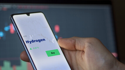 An investor's analyzing the hydrogen etf fund on screen. A phone shows the ETF's prices clean energy low carbon to invest