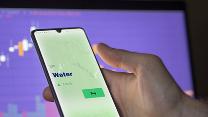 An investor's analyzing the water etf fund on screen. A phone shows the ETF's prices essential resources to invest