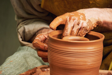 A man in old medieval Byzantine clothes sits behind a vintage potter's wheel and makes dishes out of clay. Pottery in nature in retro style.