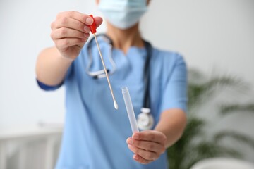 Doctor holding buccal cotton swab and tube for DNA test in clinic, closeup