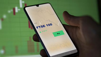 An investor's analyzing the FTSE 100 etf fund on screen. A phone shows the ETF's prices London England london ftse england to invest