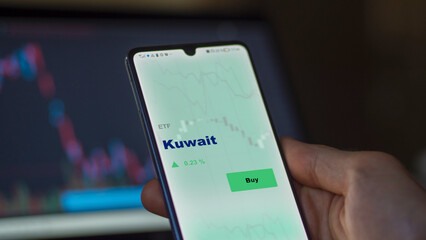 An investor's analyzing the Kuwait etf fund on screen. A phone shows the ETF's prices Kuwaiti kuwaiti kuwait to invest
