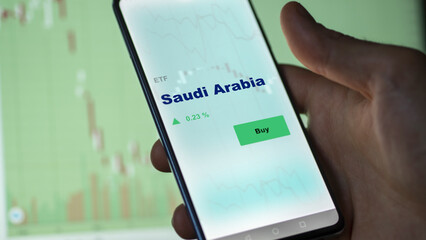 An investor's analyzing the Saudi Arabia etf fund on screen. A phone shows the ETF's prices Saudian to invest