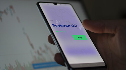 An investor's analyzing the soybean oil etf fund on screen. A phone shows the ETF's prices to invest.