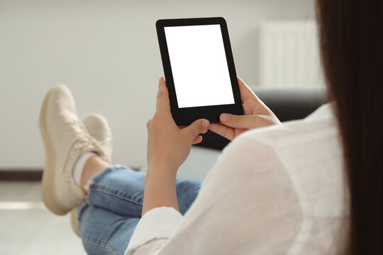 Young woman using e-book reader at home, closeup