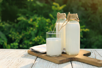 Bottles and glass of tasty fresh milk on white wooden table outdoors, space for text