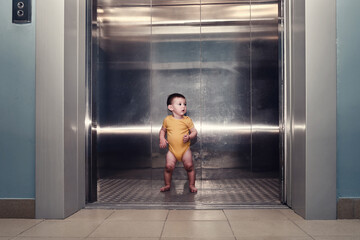 Toddler baby boy stands alone in the elevator of a residential building. A child in an elevator with the doors open. Kid age one year © Андрей Журавлев
