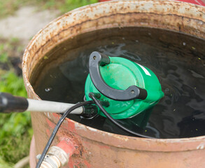 a submersible pump with an attached hose for pumping water is immersed in a metal barrel with water.