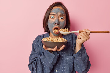 Puzzled amazed Asian woman has mouth full of cereals hears shocking news while having breakast...