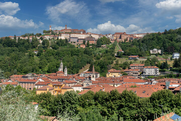 Fototapeta premium Mondovì, Cuneo, Italy: cityscape with below the Breo district and on the Mondovì hill Piazza with the clock tower and green parks with blue sky with white clouds