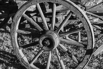 Fototapeta na wymiar This is a digitally enhanced, monochrome closeup image of a buckboard wagon wheel. The evening light and shadow accentuates the texture of the weathered wood and antique iron.