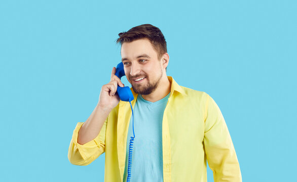 Smiling young man talk on landline phone with customer support service. Happy Caucasian male isolated on blue studio background have pleasant conversation on corded telephone. Communication.