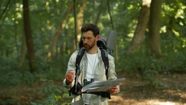 Active man tourist got lost during hiking trip in woodland, looking for right way with compass and paper map, free space