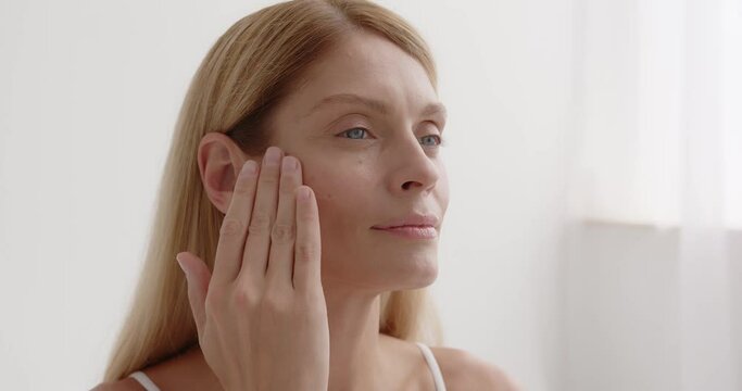 Happy mature woman using cosmetic cream to hide wrinkles below eyes
