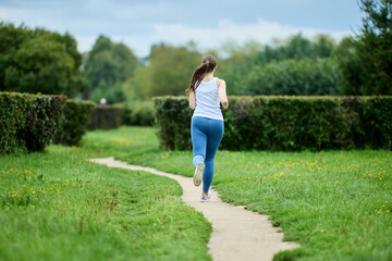 Female runner exercising in public park in summer, back view.