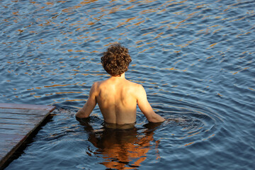 Guy with curly hair going to swim in water, back view. Beach vacation and swimming