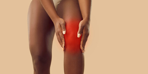 Young woman suffers from arthritis or leg injury, feels pain and touches her kneecap. Plus size...