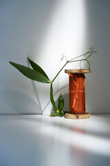 Dark orange silk ribbon on a wooden roll stand on a light background with a branch of a green plant