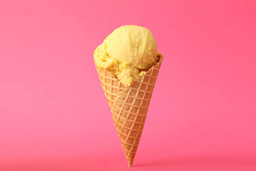 Delicious yellow ice cream in waffle cone on pink background