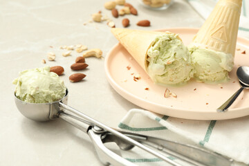 Delicious pistachio ice cream in wafer cones with chopped nuts on light table, closeup