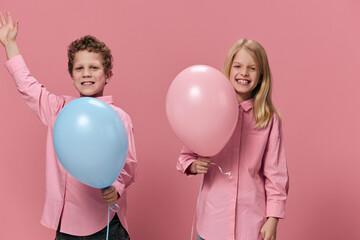 cute happy kids in pink clothes on a pink background have fun playing with colored balloons enjoying childhood