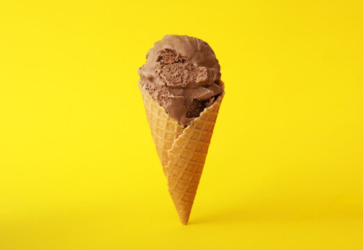 Delicious chocolate ice cream in waffle cone on yellow background