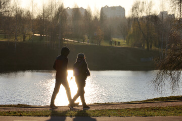 Defocused view to silhouette of couple walking along lake coast in autumn park in sunlight
