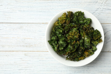 Tasty baked kale chips on white wooden table, top view. Space for text