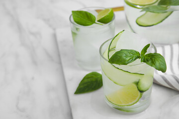 Tasty fresh cucumber water with sliced lime and basil on white marble table. Space for text