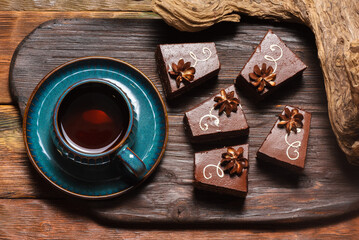 Chocolate brownie cakes and cup of black tea on the rustic wooden table background.