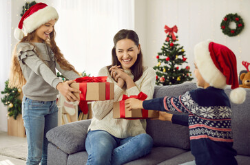 Happy family enjoying gifts on Christmas Day. Children in Santa hats giving presents to their...