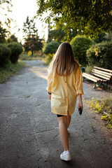 blonde girl in the yellow shirt is waking in the park on a sunny day with car keys in hands