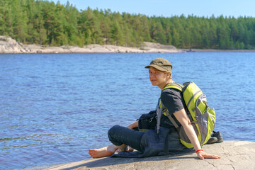 Girl tourist with a backpack sits on the shore of the lake.