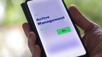 An investor's analyzing the active management etf fund on screen. A phone shows the ETF's prices stocks to invest