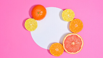Sopy space paper in circle with sliced citrus fruits around on vibrant pink background. Flat lay
