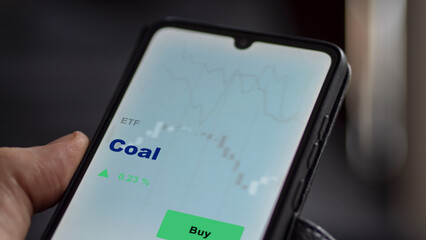 An investor's analyzing the coal etf fund on screen. A phone shows the ETF's prices energy carbon to invest