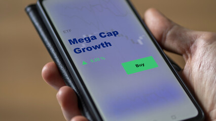 An investor's analyzing the mega cap Growth etf fund on screen. A phone shows the ETF's prices megaCap to invest