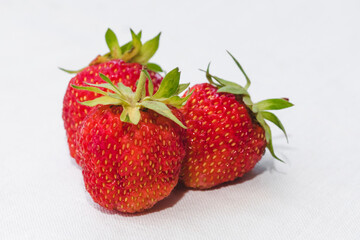 Red berry juicy strawberry. Three ripe strawberries with strawberry leaf, isolated on a white fabric background.