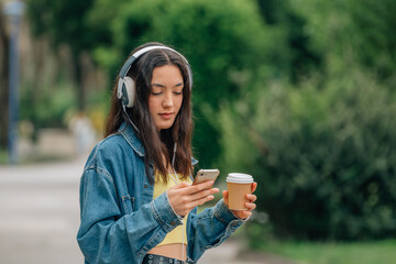 girl on the street with mobile phone and headphones and cup of coffee or soft drink