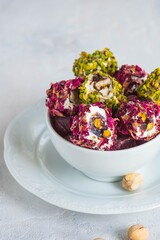 Oriental sweets, Turkish delight with rose petals and pistachios in a white bowl on a light concrete background.