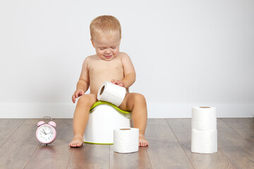 Cute baby boy sits on the potty with toilet paper in his hands. Potty training time