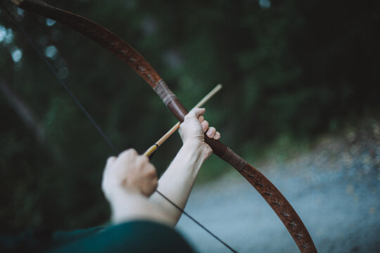 Man pulling the string of a bow, about to shoot an arrow to a forest