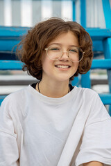 Portrait of smiling Caucasian teenage girl with curly hair in cool fashionable glasses in city park on sunny summer day