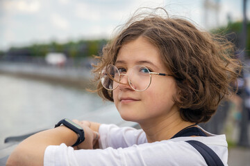 portrait of beautiful Caucasian teenage girl with curly hair in fashionable glasses in city park on sunny summer day, face close-up