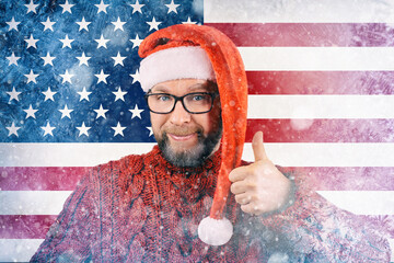 charismatic cheerful bearded man with glasses and Santa Claus hat on background of American flag covered with frost, concept of gas crisis in winter