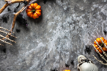 Halloween flat lay composition with pumpkins, skeleton arms, skull, spiders on stone table. Scary,...