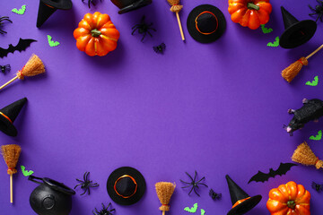 Happy Halloween holiday banner design. Frame made of Halloween decorations, orange pumpkins, witch's pots and brooms, spiders, bats on purple background. Flat lay, top view, copy space.
